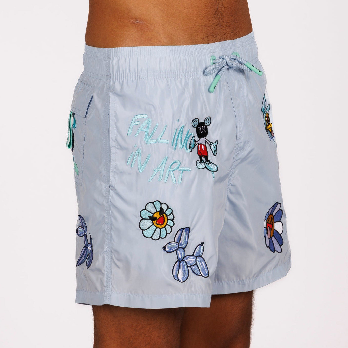 Light blue swim shorts side view with illustrated graphic and “Falling in art” text