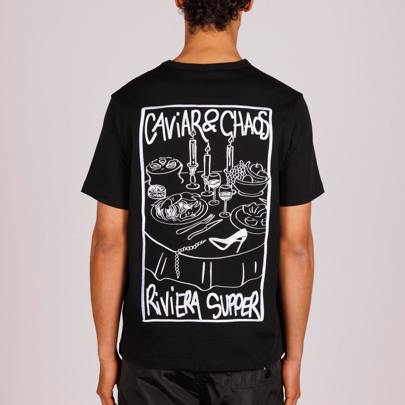 Black T-shirt back view with illustrated graphic and “Caviar&Chaos Riviera Supper” text