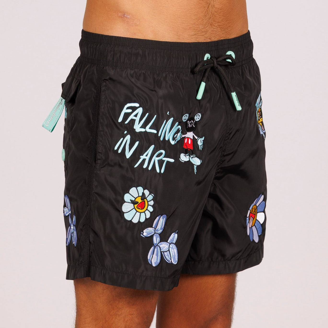 Black swim shorts side view with illustrated graphic and “Falling in art” text
